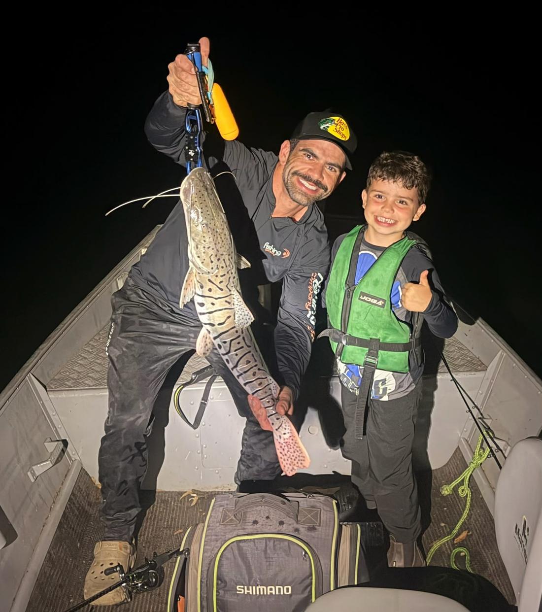 Pescador e criança segurando um grande pintado à noite no barco